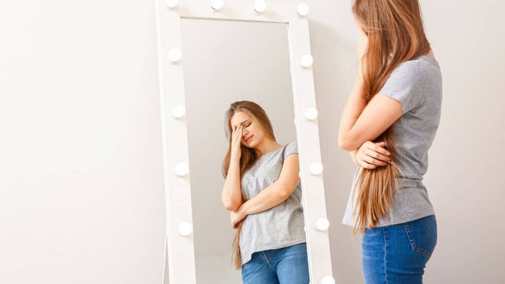 A person in front of a mirror, feeling unhappy.